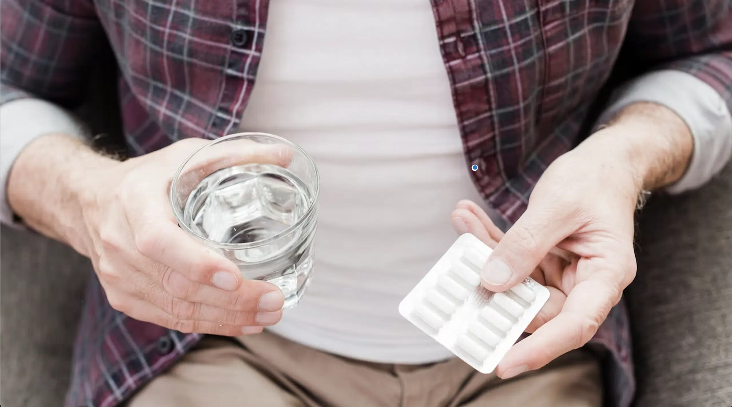 Man holding water and blister pack of pills.