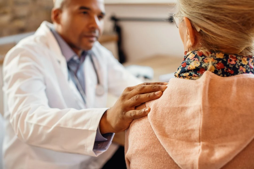 A doctor is placing a reassuring hand on the shoulder of a patient, likely offering comfort or discussing health concerns in a clinic setting.
