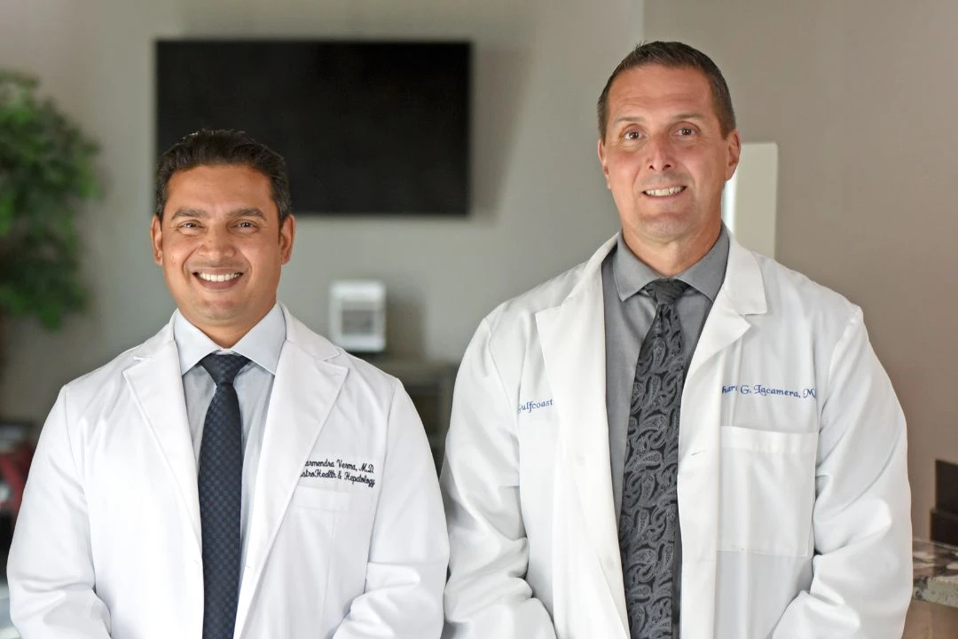 Two smiling male doctors in white coats, likely gastroenterologists, standing confidently in a medical clinic setting.