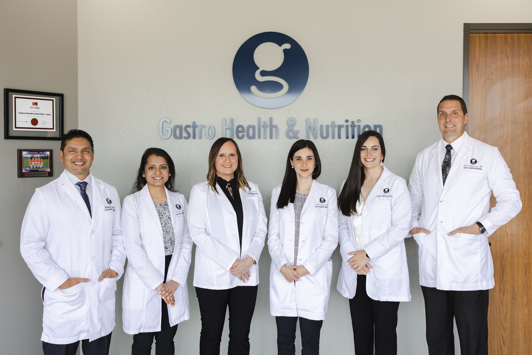 A group of medical professionals and staff, in white coats and black attire, pose for a team photo in a modern office setting.